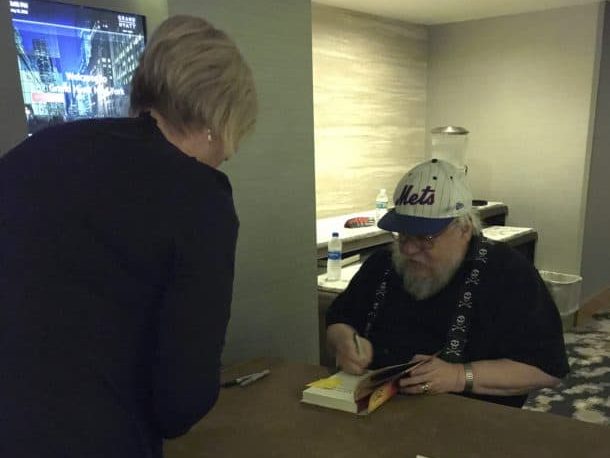 Photo of Paula Munier at a desk getting a signature on a copy by George R. R. Martin