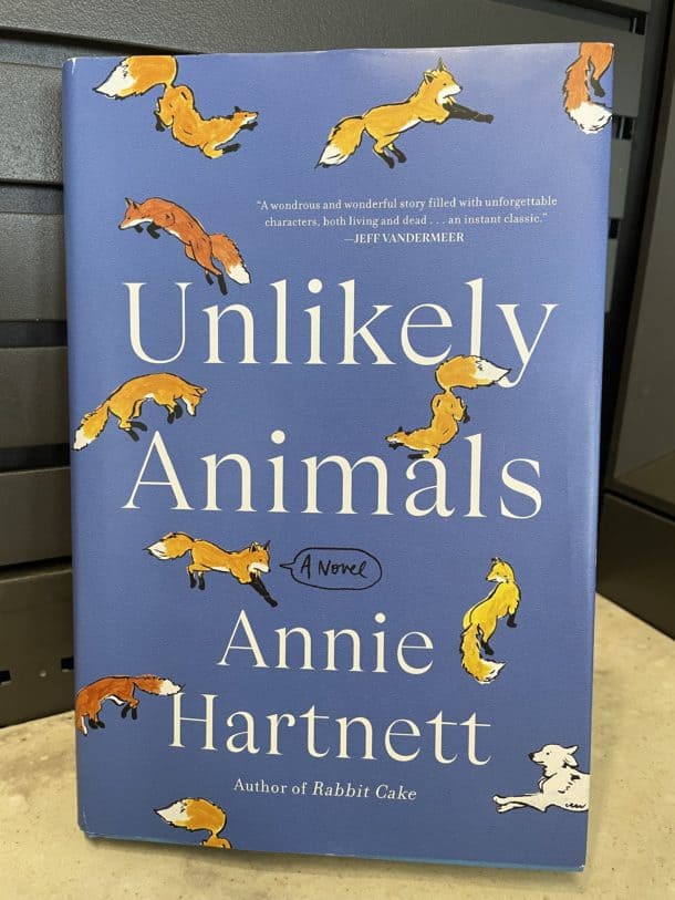 Picture of a hardcover version of Annie Hartnett's Unlikely Animals featuring a blue background and illustrated foxes in various poses